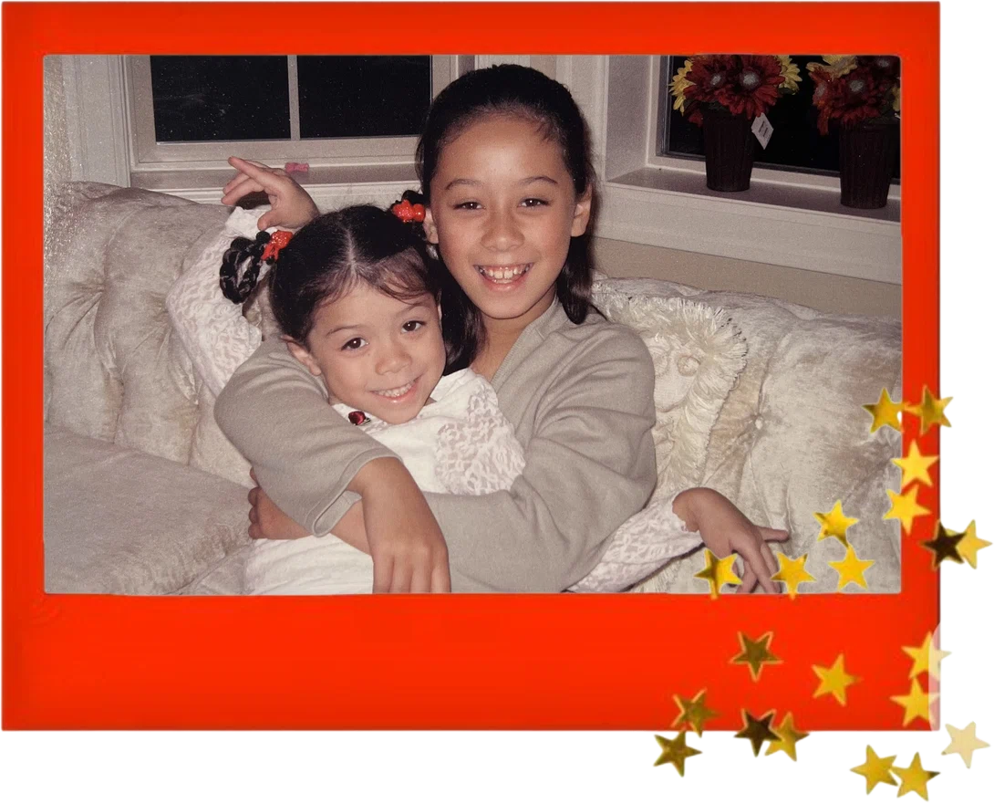 Symphony as a little girl getting a big hug from her older sister on a cream sofa, in a red photo frame with gold stars
